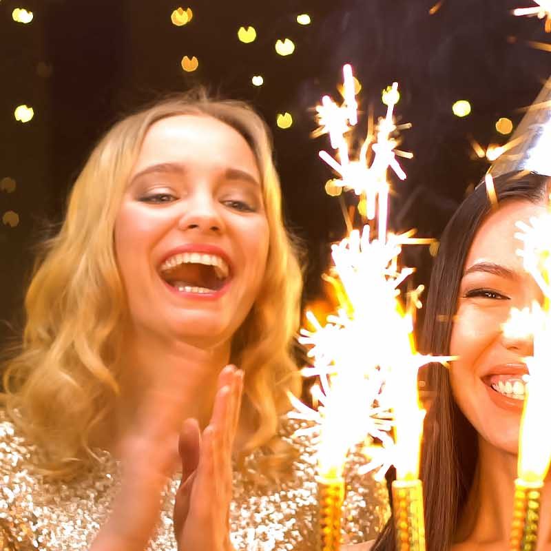 A group of young women and men celebrate with sparklers and a cake.