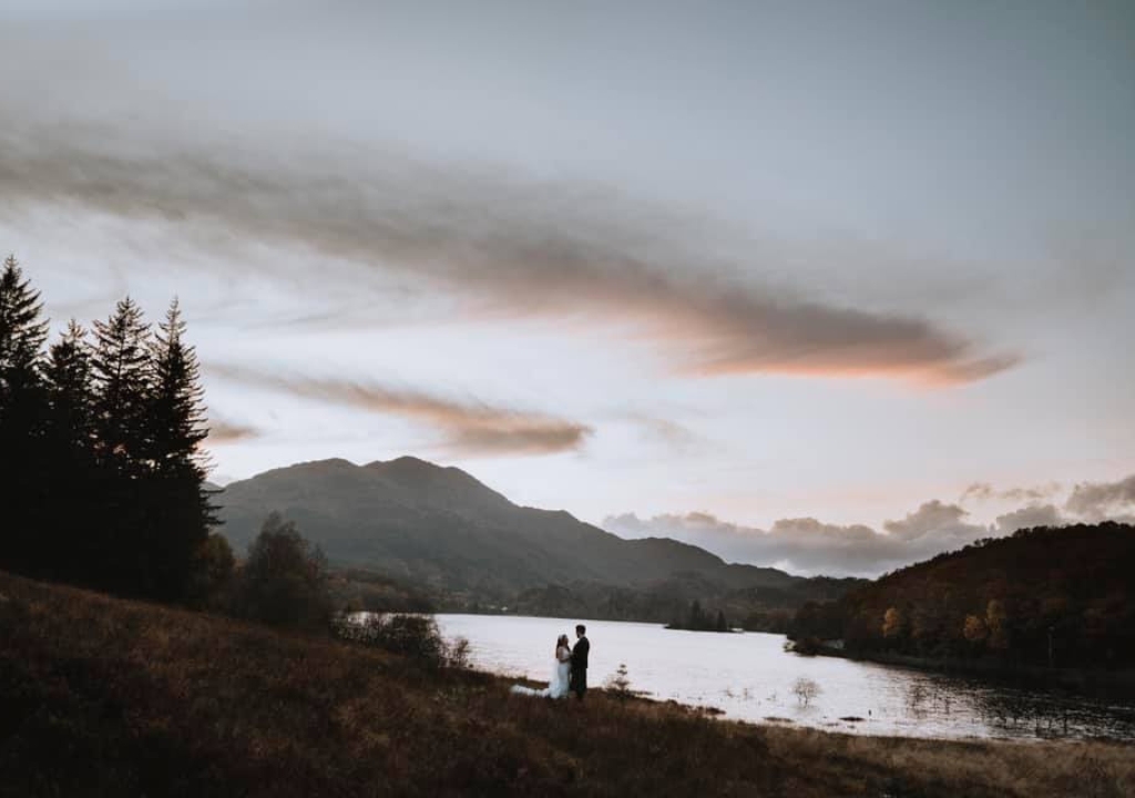 Couple facing each other on banks of loch in wedding attire