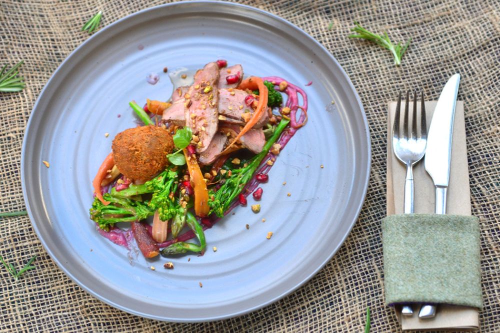 Formal main meal for event, meat with vegatables and cutlery wrapped in a napkin at the side.