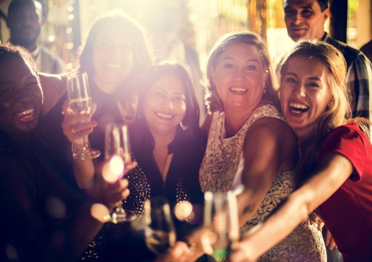People gathered together at a charity ball, with drinks in flute glasses smiiling and dancing together.